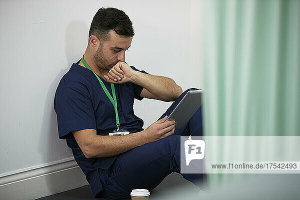 Healthcare worker looking at tablet PC sitting by wall in medical room