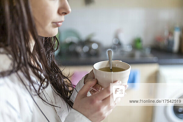 Woman holding tea cup in kitchen at home