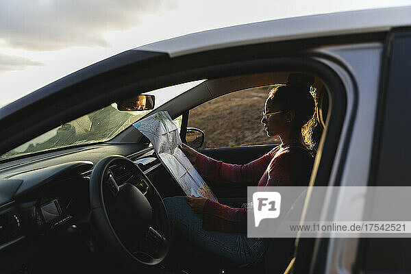 Young woman checking map in car at sunset