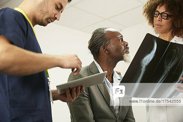 Nurse with tablet PC by patient listening to doctor explaining X-ray in medical room