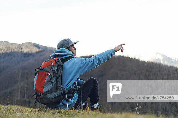Hiker with backpack pointing at clear sky