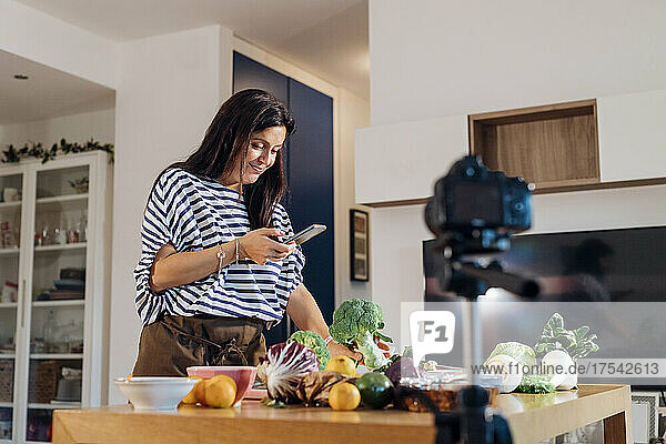 Woman using smart phone filming tutorial through camera at home