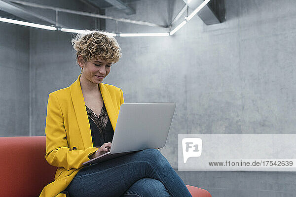 Smiling businesswoman using laptop sitting on sofa at office