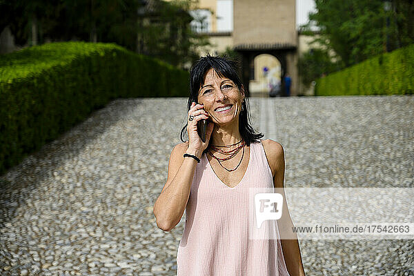 Lächelnde Frau  die an einem sonnigen Tag über ihr Mobiltelefon spricht