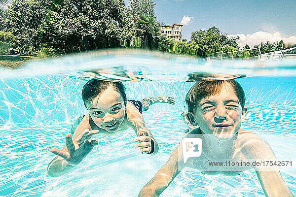 Smiling siblings swimming underwater in pool on sunny day