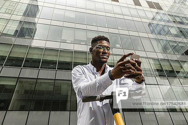 Young man using smart phone in front of glass building