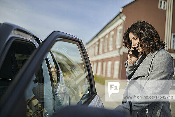Woman talking on mobile phone and opening car door