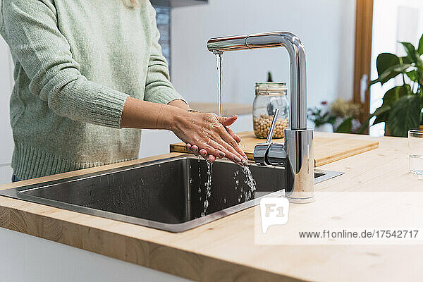 Woman washing hands in kitchen at home