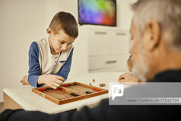 Concentrated boy playing backgammon with grandfather at home