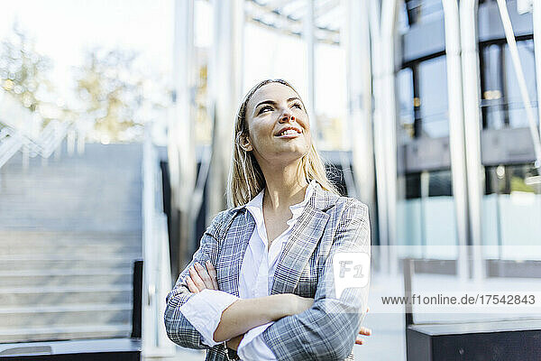 Smiling young businesswoman day dreaming with arms crossed