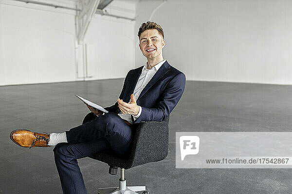 Young businessman with tablet PC on chair at industial hall