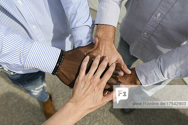 Multiracial friends doing stacking hands on footpath