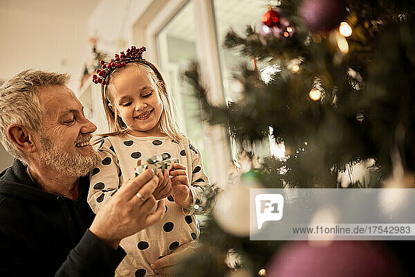Grandfather and granddaughter decorating christmas tree at home