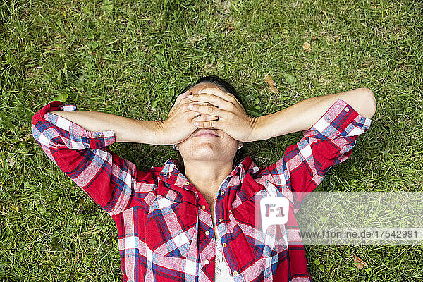 Woman covering eyes with hands lying on grass