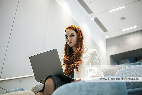 Confident working woman using laptop sitting in convention center