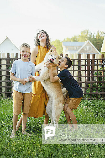 Cheerful family with their Akita dog standing on grass in front of fence
