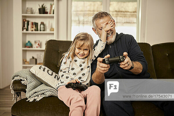 Granddaughter playing video game with grandfather at home