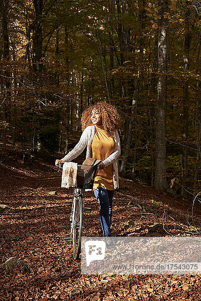 Frau geht an einem sonnigen Tag im Herbstwald mit dem Fahrrad spazieren