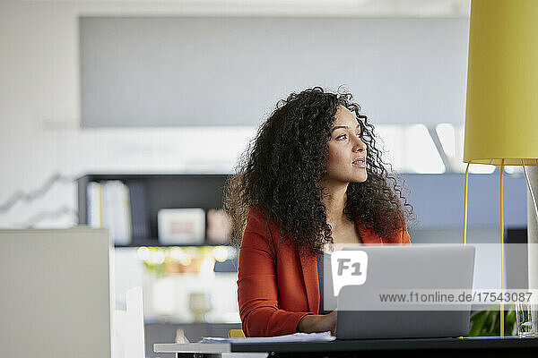 Contemplative businesswoman with laptop at desk in office