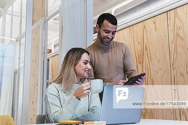 Businesswoman holding cup with colleague using tablet PC at studio