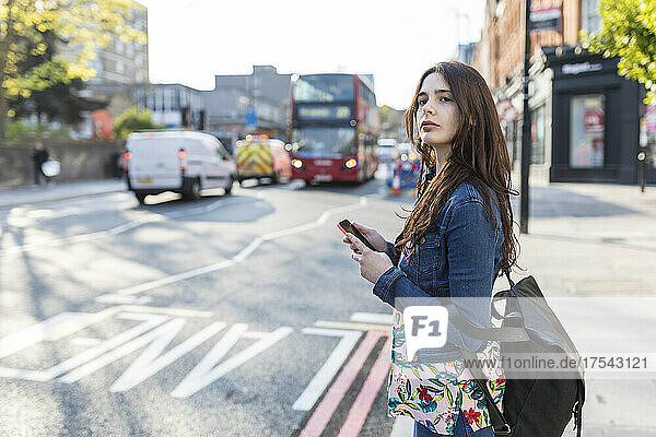 Frau mit Smartphone wartet am Straßenrand in der Stadt