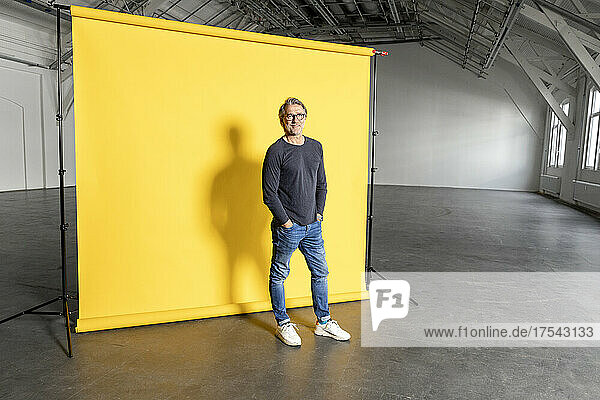 Businessman with hands in pockets at yellow backdrop
