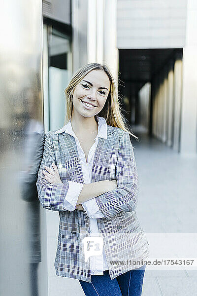 Smiling working woman with arms crossed leaning on wall