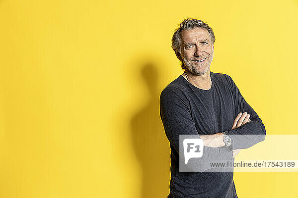 Smiling businessman with arms crossed in front of yellow background