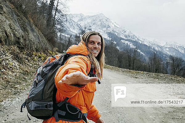 Cheerful man in orange jacket walking on mountain road