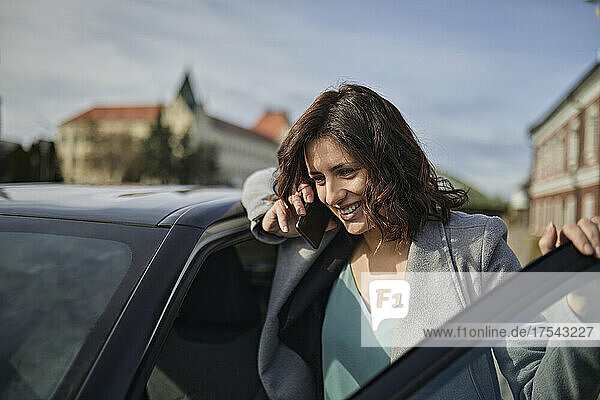 Smiling woman talking on mobile phone at car door