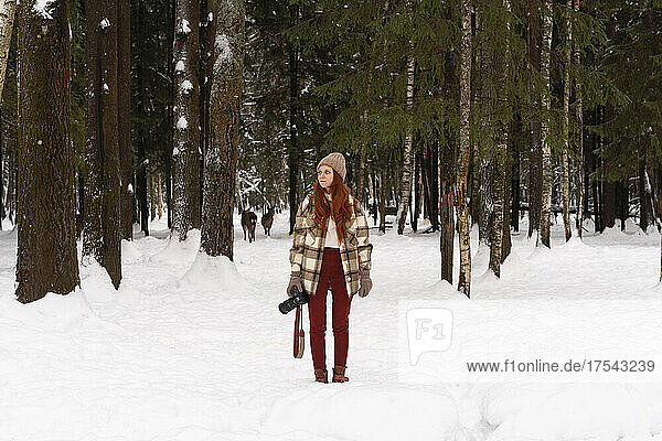 Woman with camera standing on snow in winter forest