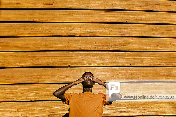 Man with hands covering eyes in front of orange wall at sunset