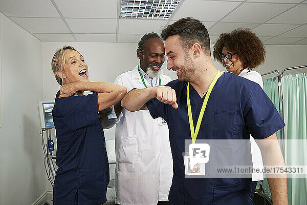 Playful medical colleagues giving elbow bump in medical room