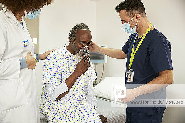 Mitarbeiter des Gesundheitswesens trösten Patienten mit Sauerstoffmaske im Krankenzimmer