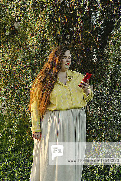 Plus size woman using smart phone in front of plants