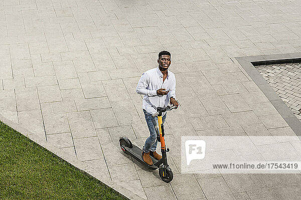 Young man with electric push scooter on footpath