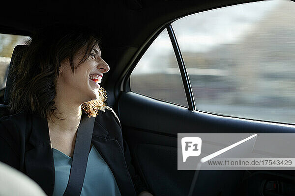 Happy businesswoman with laptop traveling in car