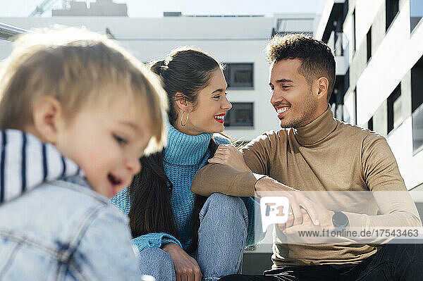 Happy parents looking at each other by son on sunny day