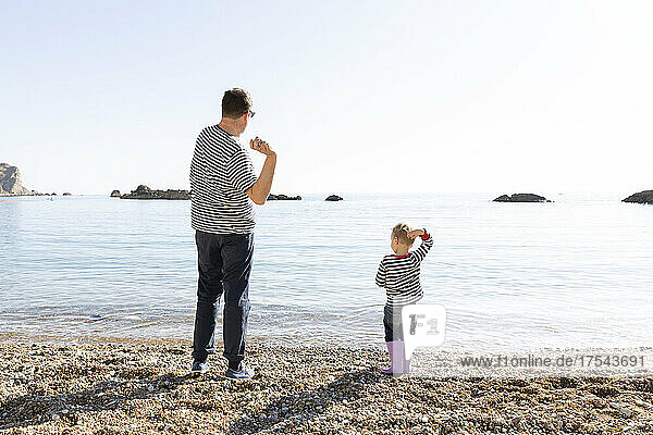 Rear view of father and son (18-23 months) skipping stones on lakeshore