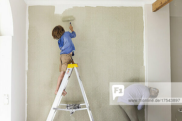 A woman and an eight year old boy decorating a room  painting walls.