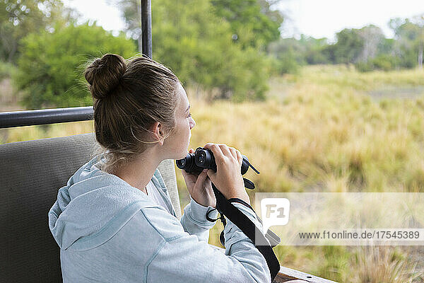 Africa  Zambia  Girl (16-17) in safari vehicle using binoculars
