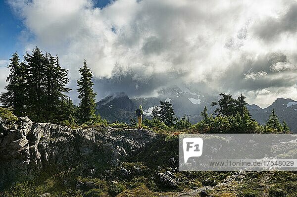 Hiker in front of cloudy Mt. Shuksan with snow and glacier  dramatic cloudy sky  Mt. Baker-Snoqualmie National Forest  Washington  USA  North America