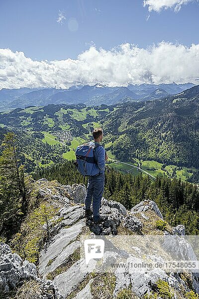 Wanderer steht auf einem Felsen  Blick ins Tal bei Sachrang  Wanderung zum Geigelstein im Frühling  Chiemgauer Alpen  Bayern  Deutschland  Europa