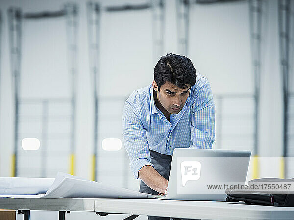 Indian architect using laptop in empty warehouse