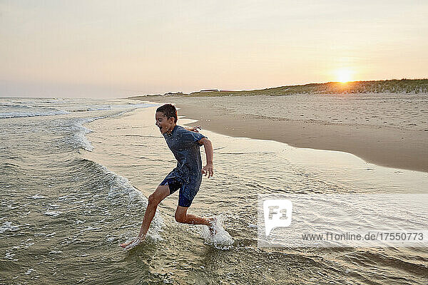Smiling boy (8-9) playing in sea waves at sunset