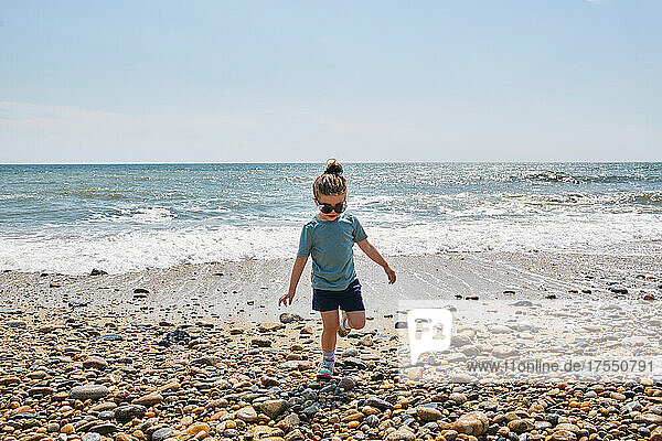 Girl (2-3) wearing sunglasses walking on pebbled beach