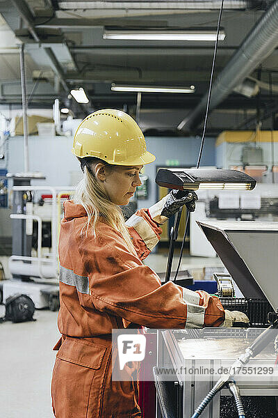 Young female industrial worker in uniform using manufacturing machinery at factory