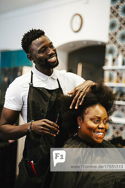 Lächelnder männlicher Friseur  der einer Kundin im Salon die Haare schneidet
