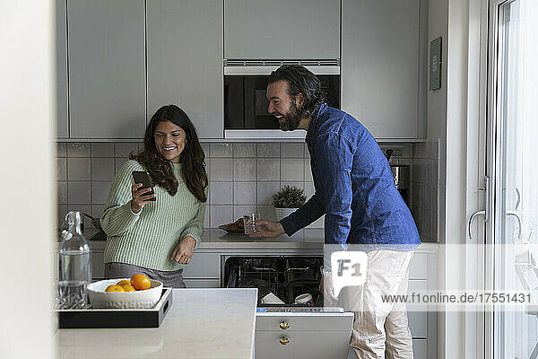 Lächelnde Frau teilt Smartphone mit Mann in Küche