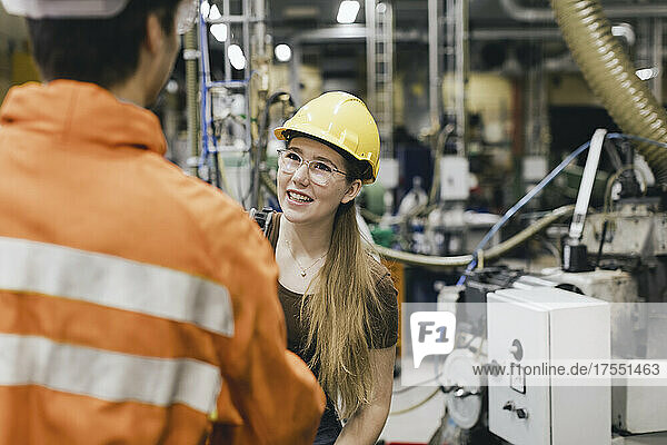 Smiling female manager wearing hardhat talking with male worker in factory